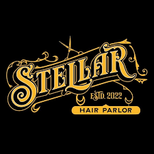 A vintage-style graphic logo for "Stellar Hair Parlor," established in 2022. The design features bold, stylized gold lettering with intricate filigree and ornate flourishes against a solid black background. A pair of open salon scissors is integrated into the top scrollwork, and the words "HAIR PARLOR" are enclosed in a smooth gold banner at the bottom.